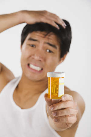 Frustrated Asian man holding medication bottleの写真素材