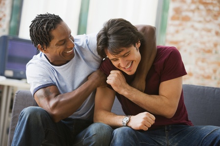 Multi-ethnic men hugging on sofaの写真素材
