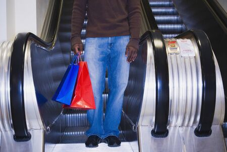 African man on escalator with shopping bagsの写真素材