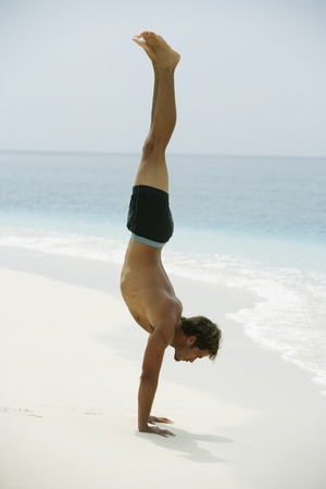 South American man doing handstand at beach