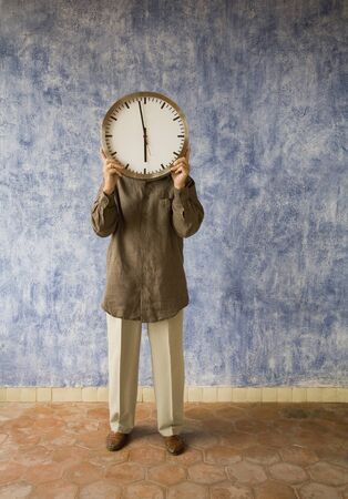 Senior man holding clock over faceの写真素材