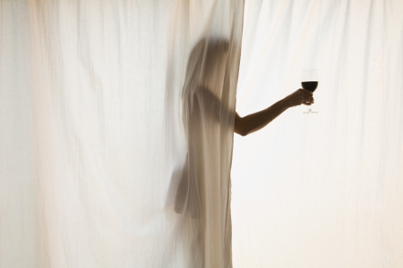 Hispanic woman holding wine glass in curtainsの写真素材