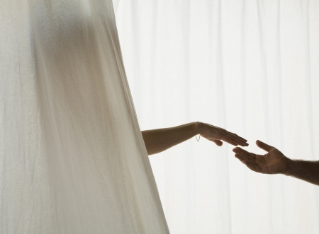 Hispanic couple reaching for each other through curtainの写真素材