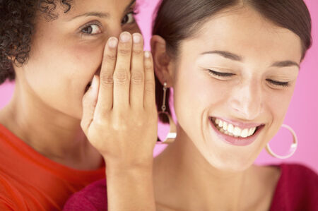 Portrait of a young women whispering into a woman's ear