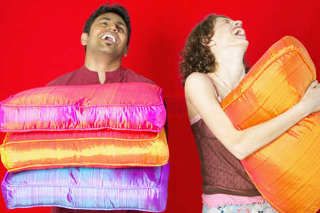 Young couple holding cushions laughingの写真素材