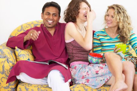 Two young women laughing sitting on a couch with a young man
