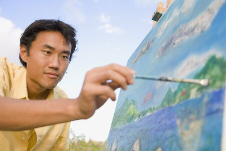 Asian man painting at easel outdoors, Florianopolis, Brazilの写真素材