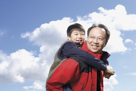 Asian father giving son piggyback ride outdoorsの写真素材