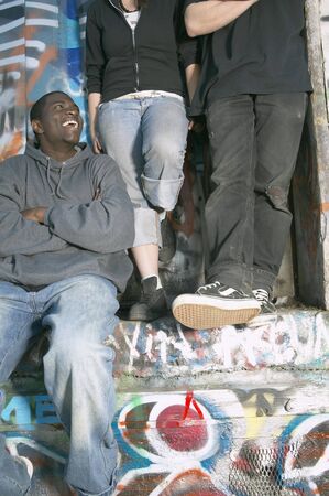 Group of young adults leaning against graffitied wallの写真素材