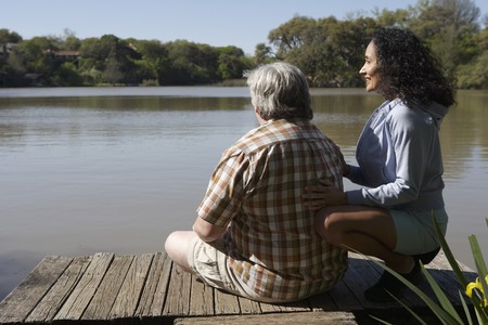 Couple sitting on wooden dock looking at waterの写真素材