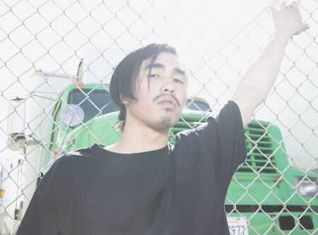Young Asian man leaning against metal fenceの写真素材