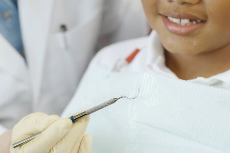 Close up of dentist's hand holding dental tool next to boy's mouthの写真素材