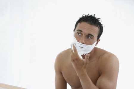 Man with bare chest applying shaving cream to faceの写真素材