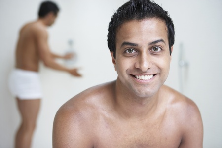 Indian man with bare chest smiling while man in underwear tests shower in backgroundの写真素材