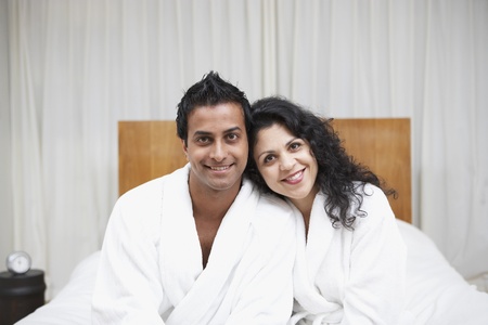 Middle Eastern couple smiling in bathrobes on bedの写真素材