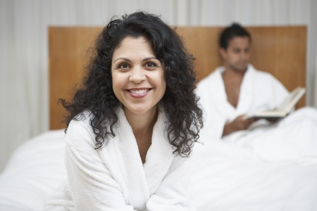 Middle Eastern woman in bathrobe with man reading in bedの写真素材