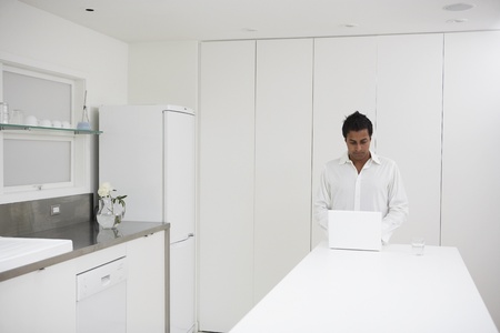 Man using laptop on counter in kitchenの写真素材