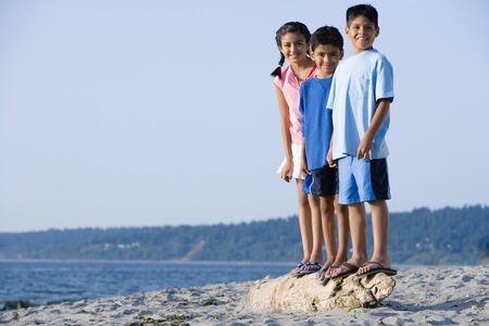 Hispanic siblings standing on driftwood at beachの写真素材