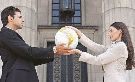 Businesspeople holding globe in front of buildingの写真素材