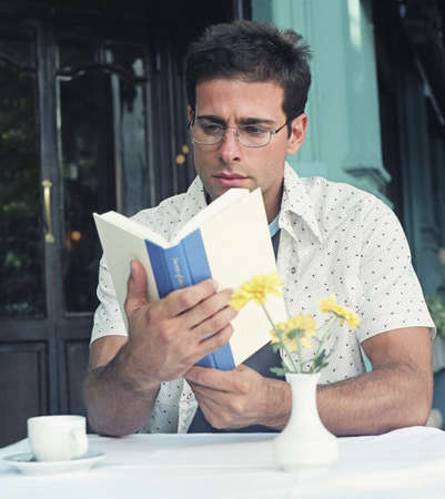 Hispanic man reading book at outdoor cafe