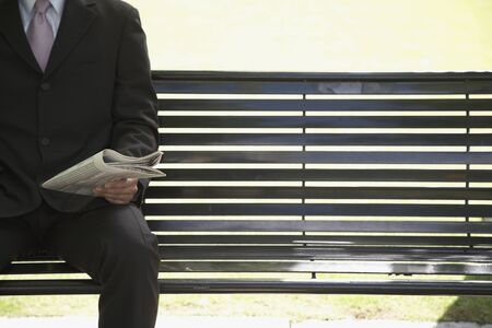 Businessman reading newspaper on park benchの写真素材