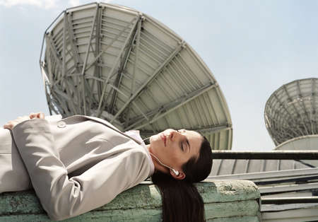 Hispanic businesswoman wearing earbuds next to satellite dishes