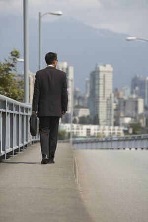 Asian businessman walking on urban bridgeの写真素材