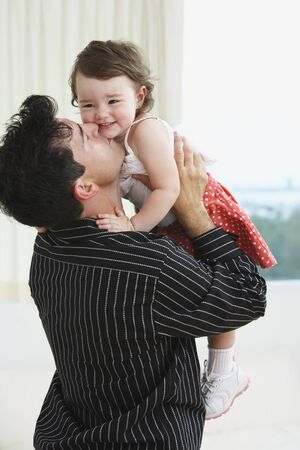 Hispanic father holding up and kissing young daughterの写真素材