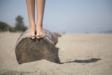 Close up of girl standing barefoot on log at beachの写真素材