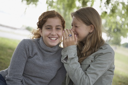 Two teenage girls telling secrets outdoors