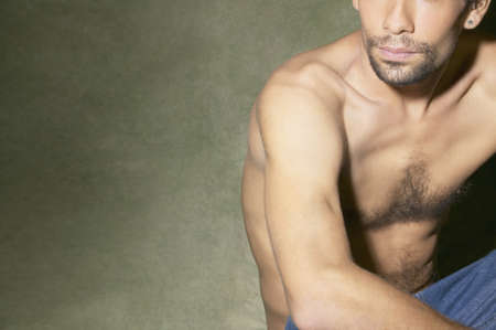 Bare-chested Hispanic man sitting on floor