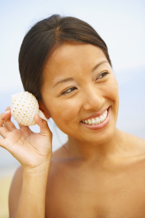 Asian woman listening to seashell