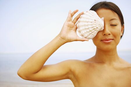 Asian woman holding seashell over eyeの写真素材