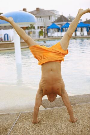 Man performing handstand next to swimming pool