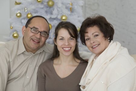 Hispanic parents and adult daughter next to Christmas treeの写真素材