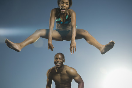 African American woman in bathing suit jumping over manの写真素材