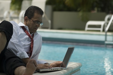 Hispanic businessman using laptop next to swimming pool