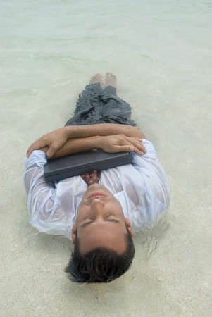 Hispanic businessman hugging laptop in water