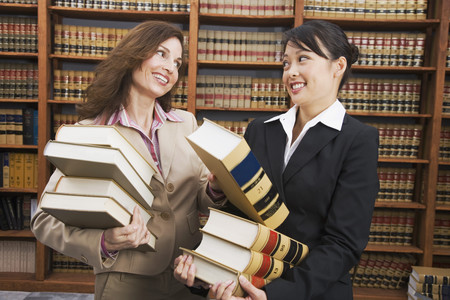 Multi-ethnic women carrying stacks of library reference booksの写真素材
