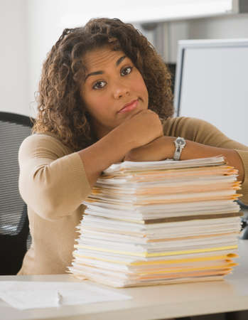 African businesswoman leaning on stack of paperwork