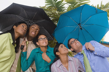 Hispanic businesspeople standing under umbrellasの写真素材