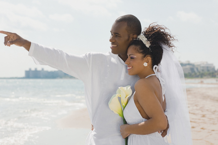 Multi-ethnic bride and groom pointing at beachの写真素材