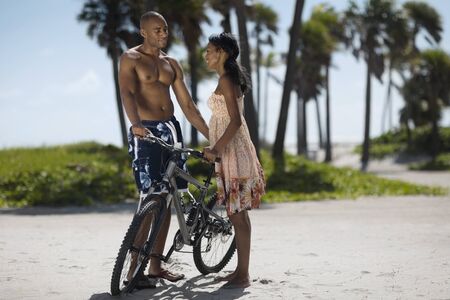 Multi-ethnic couple with bicycle at beachの写真素材