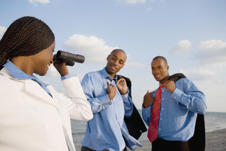 African businesswoman looking through binoculars at co-workersの写真素材