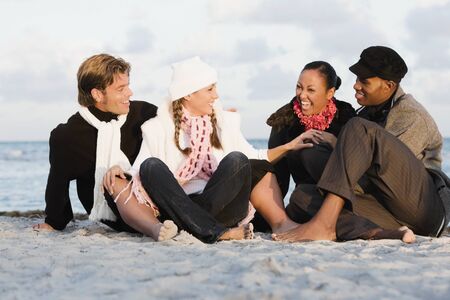 Multi-ethnic couples sitting on beachの写真素材