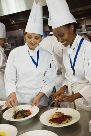 Multi-ethnic female chefs garnishing plates of food