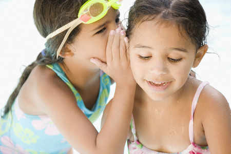 Hispanic girl whispering to sisterの写真素材