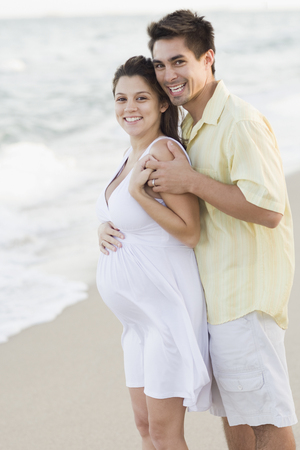 Husband hugging pregnant wife on beachの写真素材