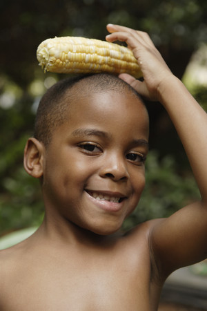 African American boy holding ear of corn on headの写真素材