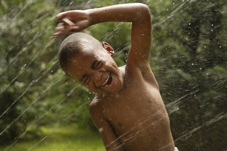 African American boy playing in sprinklerの写真素材